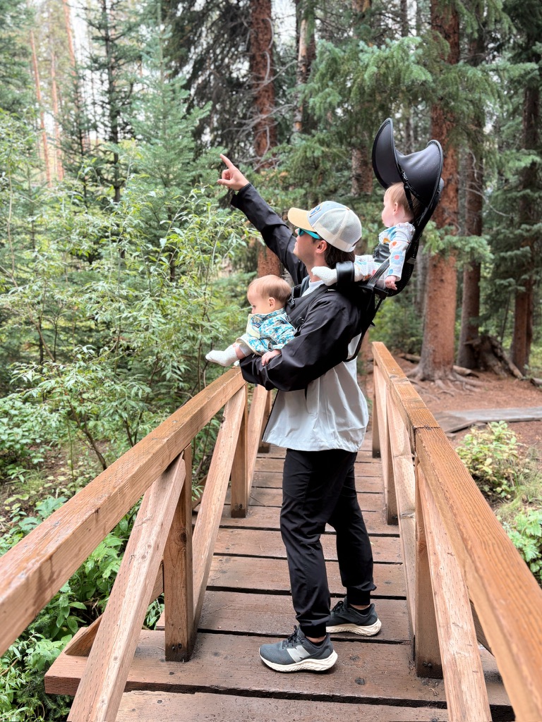 John Mulhern hiking with his twin daughters on a wooded bridge.