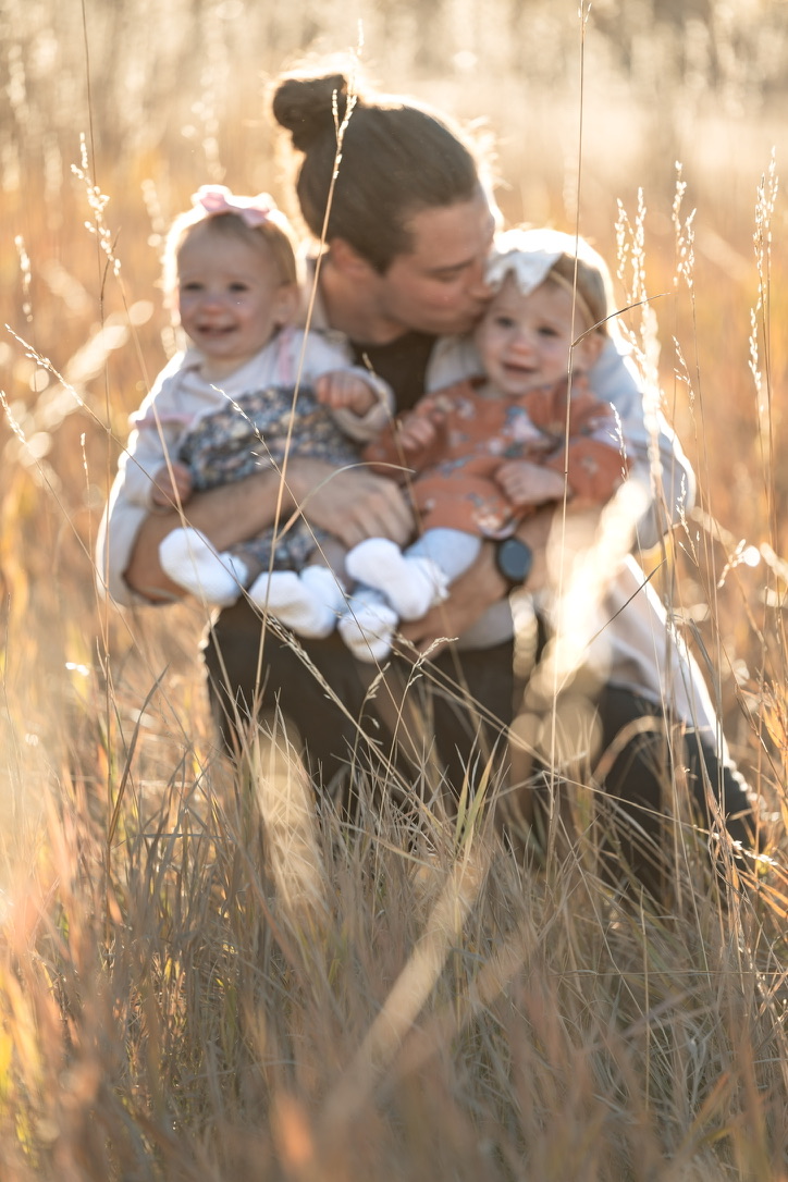 John with his twin daughters in a field.
